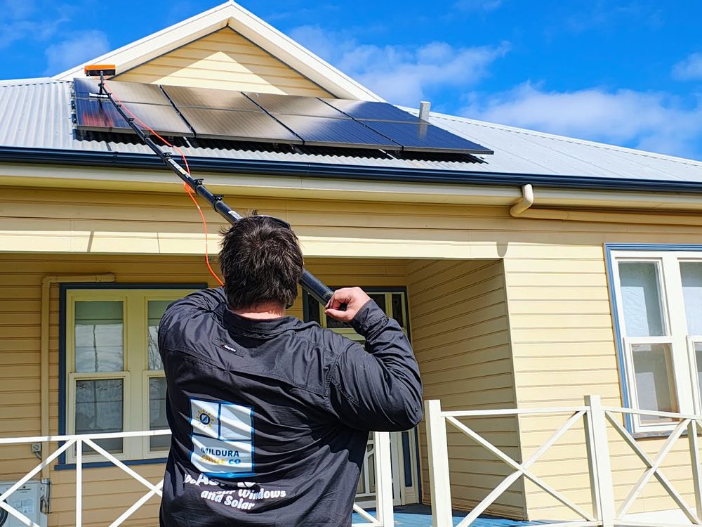 James, owner of Mildura Shine Co, in a branded jacket cleaning a rooftop solar array from the ground with a water-fed pole