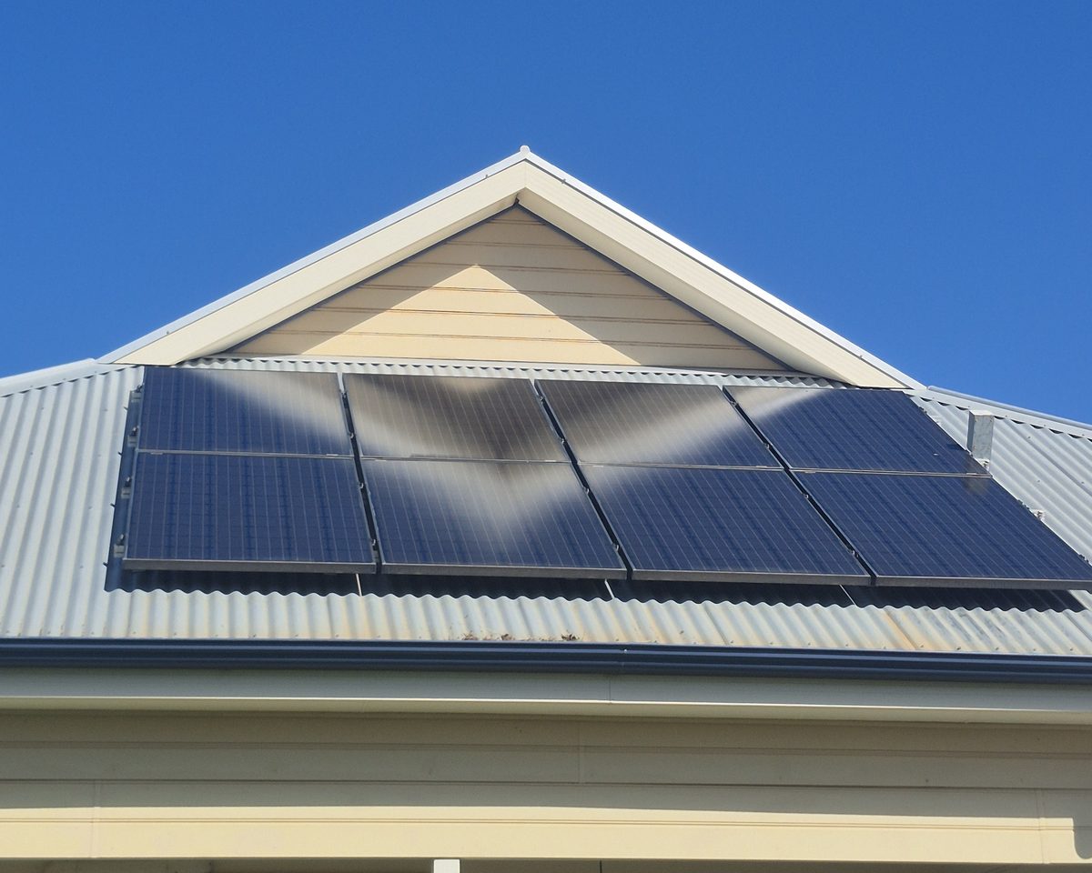 The same eight-panel solar array after cleaning, seen from the ground under a clear blue sky