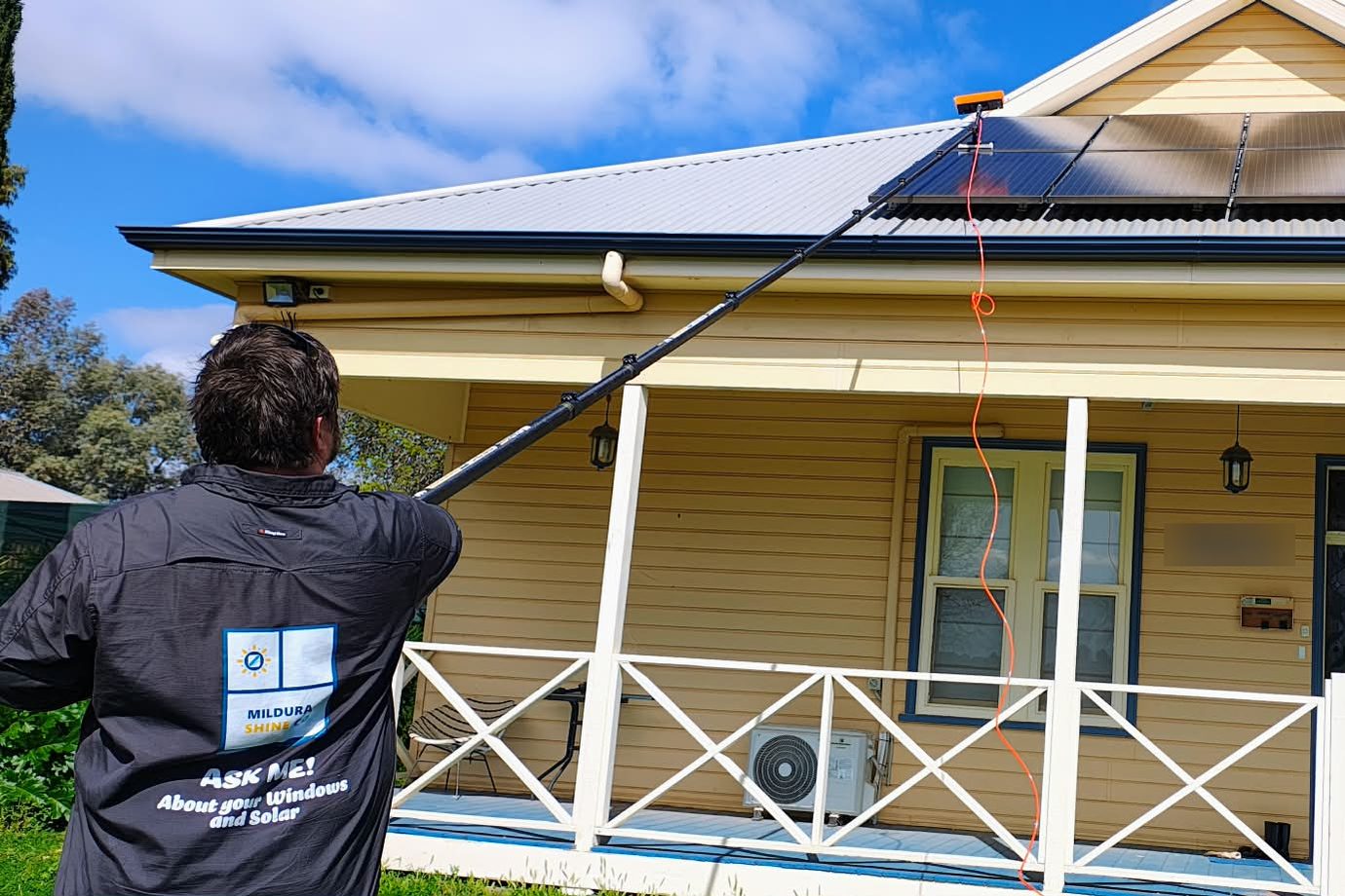James from Mildura Shine Co cleaning a rooftop solar array from the ground with a water-fed pole on a single-storey weatherboard home in Sunraysia